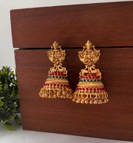 Gold earrings with red and green stones on a wooden box