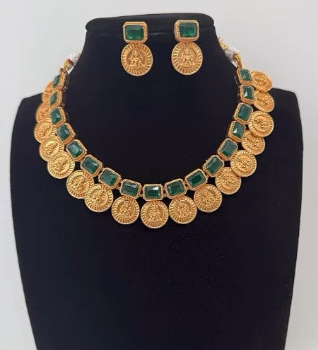 Gold necklace with green stones and matching earrings on a black stand.